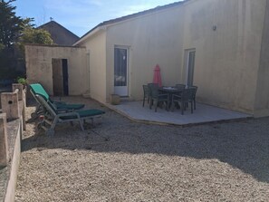 Un patio con una mesa y sillas, una zona de estar cubierta y dos sillones.