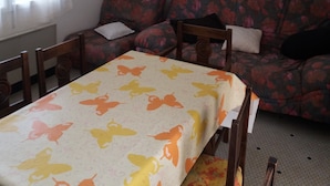 A dining area with a table covered in a butterfly-patterned tablecloth, a floral sofa, and a ceiling fan. - Single-storey house type III, 80 m from the sea and 10 mins from the town center (Préfailles)
