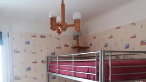 A bunk bed room with a wooden ceiling fan, a small bedside table with a lamp, and a wall with maritime-themed wallpaper. - Single-storey house type III, 80 m from the sea and 10 mins from the town center (Préfailles)