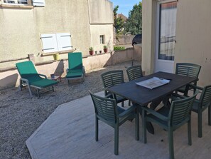 Un patio al aire libre con una mesa, sillas, una ventana con persianas y plantas en macetas.