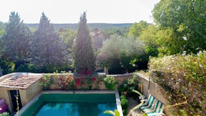 Une piscine bordée d’un mur de pierre et entourée de verdure, un bâtiment en pierre en arrière-plan et une vue sur une zone boisée.