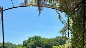 A patio with a metal table and chairs, a stone wall, and a view of a vineyard. - Les Clairians, house in the vineyards, swimming pool (Le Cannet-des-Maures)
