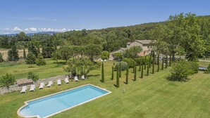 A swimming pool surrounded by a well-maintained lawn, a stone wall, and a row of sun loungers.