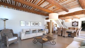 A spacious living area with a high ceiling, a dining table set for four, and a staircase leading to another level.