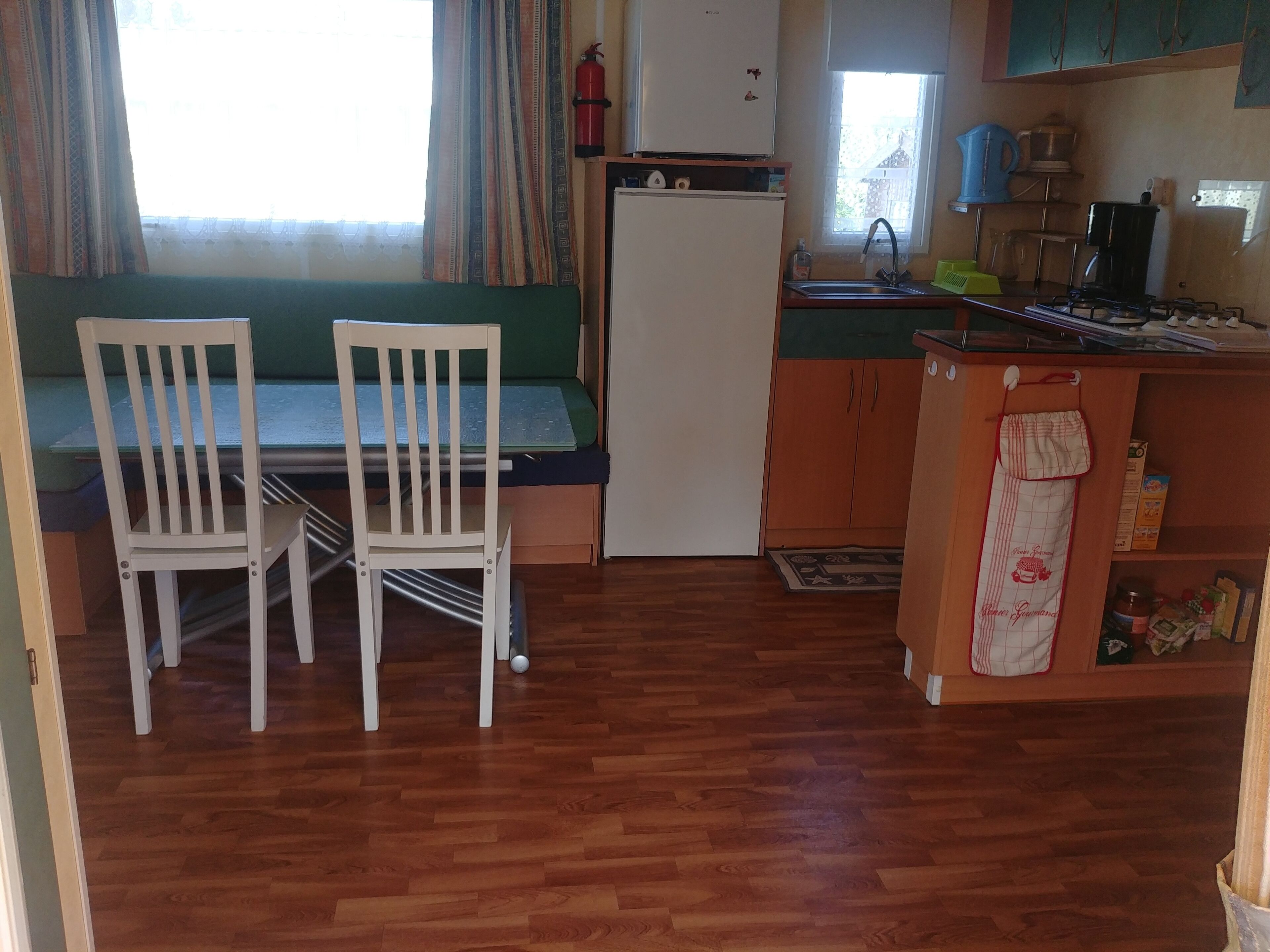 A compact kitchen with a dining area, wooden flooring, and a window with curtains.