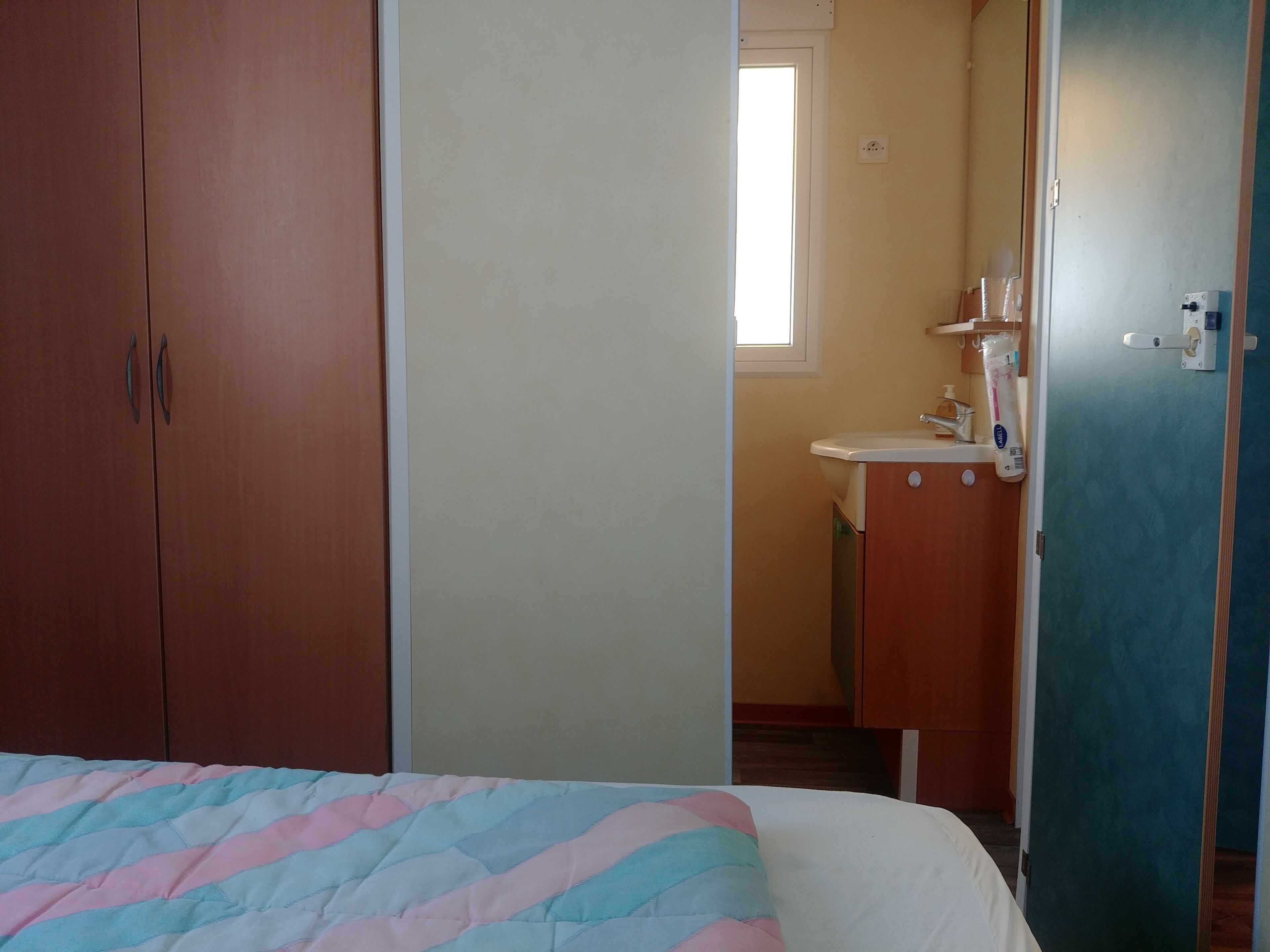 Un dormitorio con cama, armario y baño visible a través de una puerta abierta.