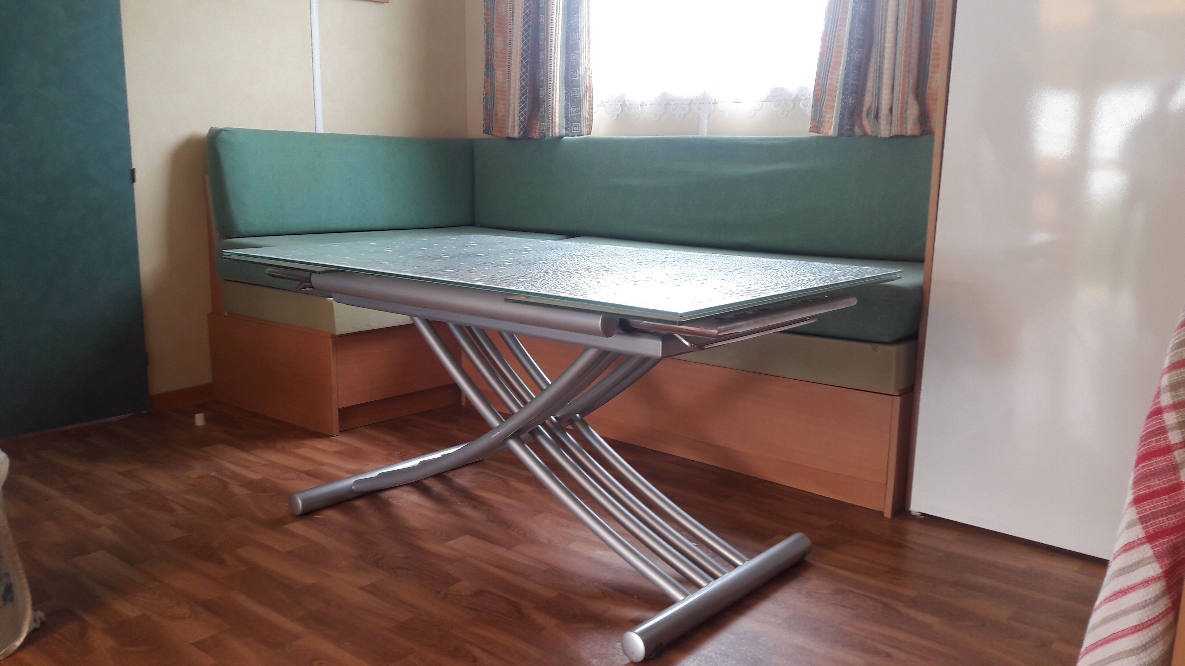 A compact room with a green cushioned bench, a foldable metal table, and a wooden floor.