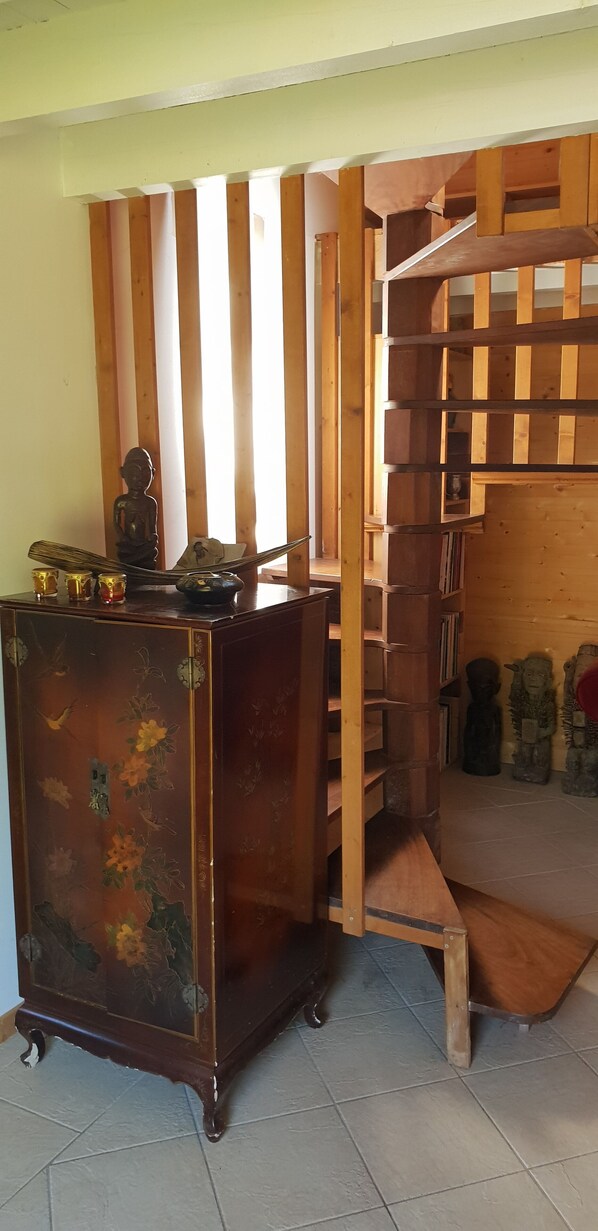 Um quarto com escada de madeira, um armário de madeira com detalhes decorativos e piso de azulejos.