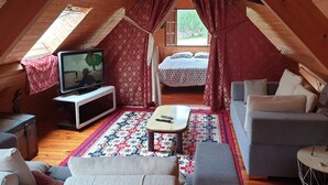 A cozy attic room with a television, a sofa, a bed, and a patterned rug.