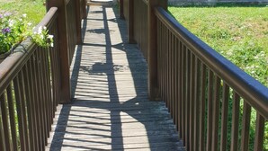 A wooden covered walkway with railings, leading to a building with a tiled roof.