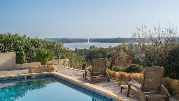 A swimming pool with two chairs and a view of a distant fountain. - A haven of peace nestled in the heart of Provence (Istre)