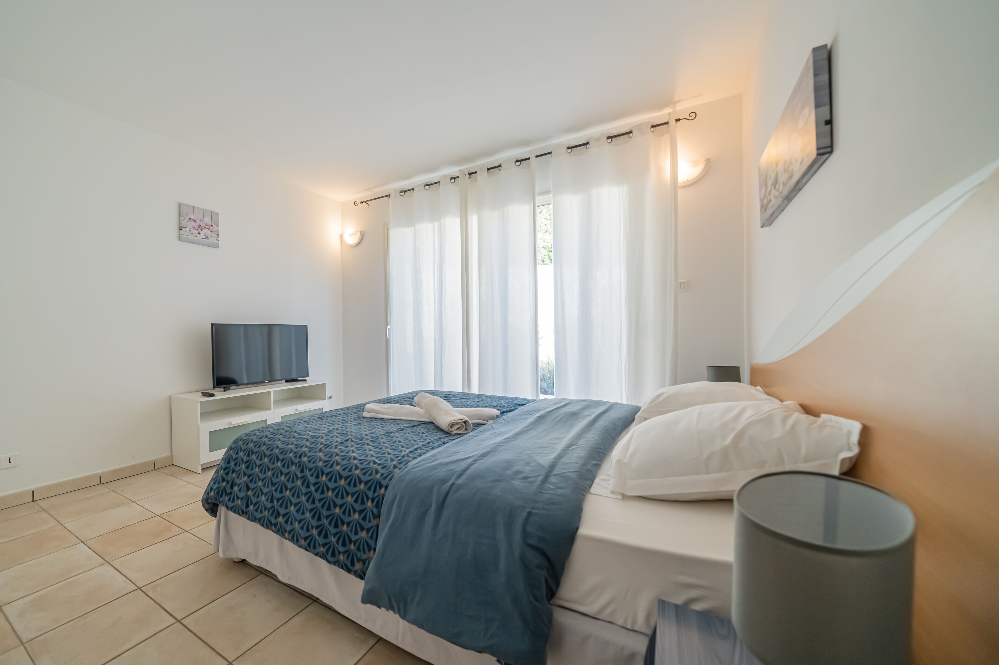 Une chambre à coucher avec un lit, une télévision, une table de chevet et une lampe.
