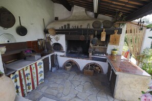 Une cuisine rustique avec un sol en pierre, un four en briques et divers ustensiles de cuisine.