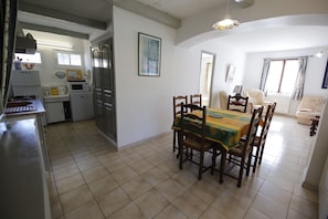 Une cuisine compacte dotée d’appareils électroménagers modernes, un coin repas avec une table et des chaises, et un salon avec un canapé et une fenêtre.