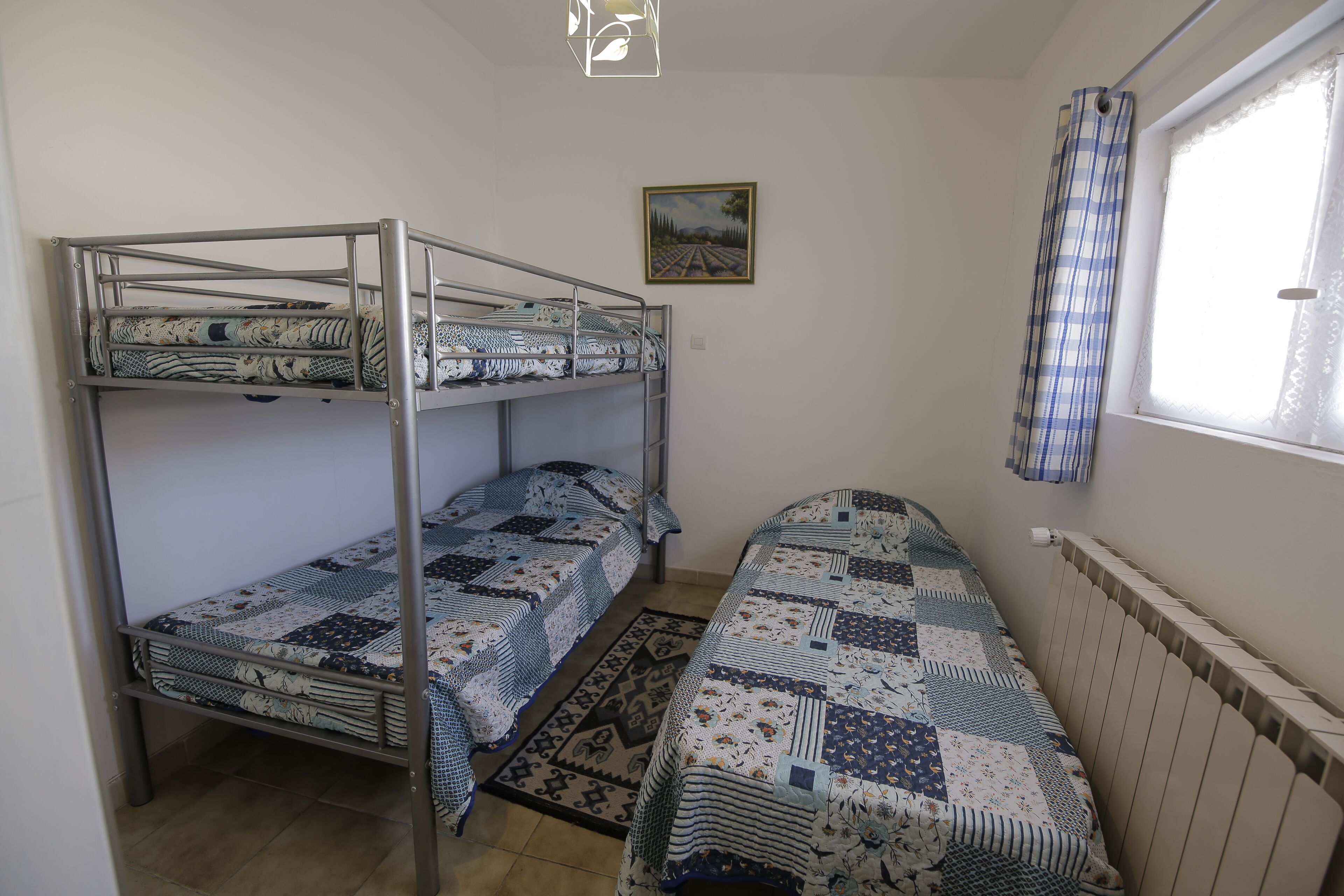 Une chambre de dortoir avec des lits superposés, un tapis à motifs, une fenêtre avec un rideau et un tableau accroché au mur.