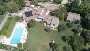 Vue aérienne d’un quartier résidentiel avec une piscine, des panneaux solaires et des maisons aux toits de tuiles.