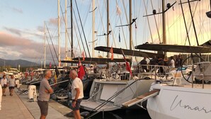 Una marina amb diverses embarcacions amarrades, una passarel·la de fusta i persones passejant.