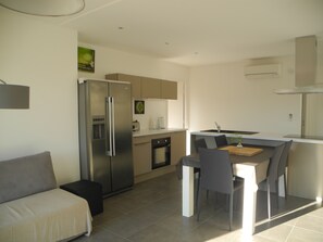 A modern kitchen with a refrigerator, stove, and sink. There is a dining area with a table and chairs. - Apartment 80 m², 2 bedrooms, 5/7 pers, garden 900 m², swimming pool (Saint-Florent)