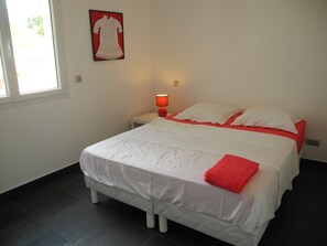 Een slaapkamer met een bed, nachtkastje, lamp, raam en een lijst aan de muur.