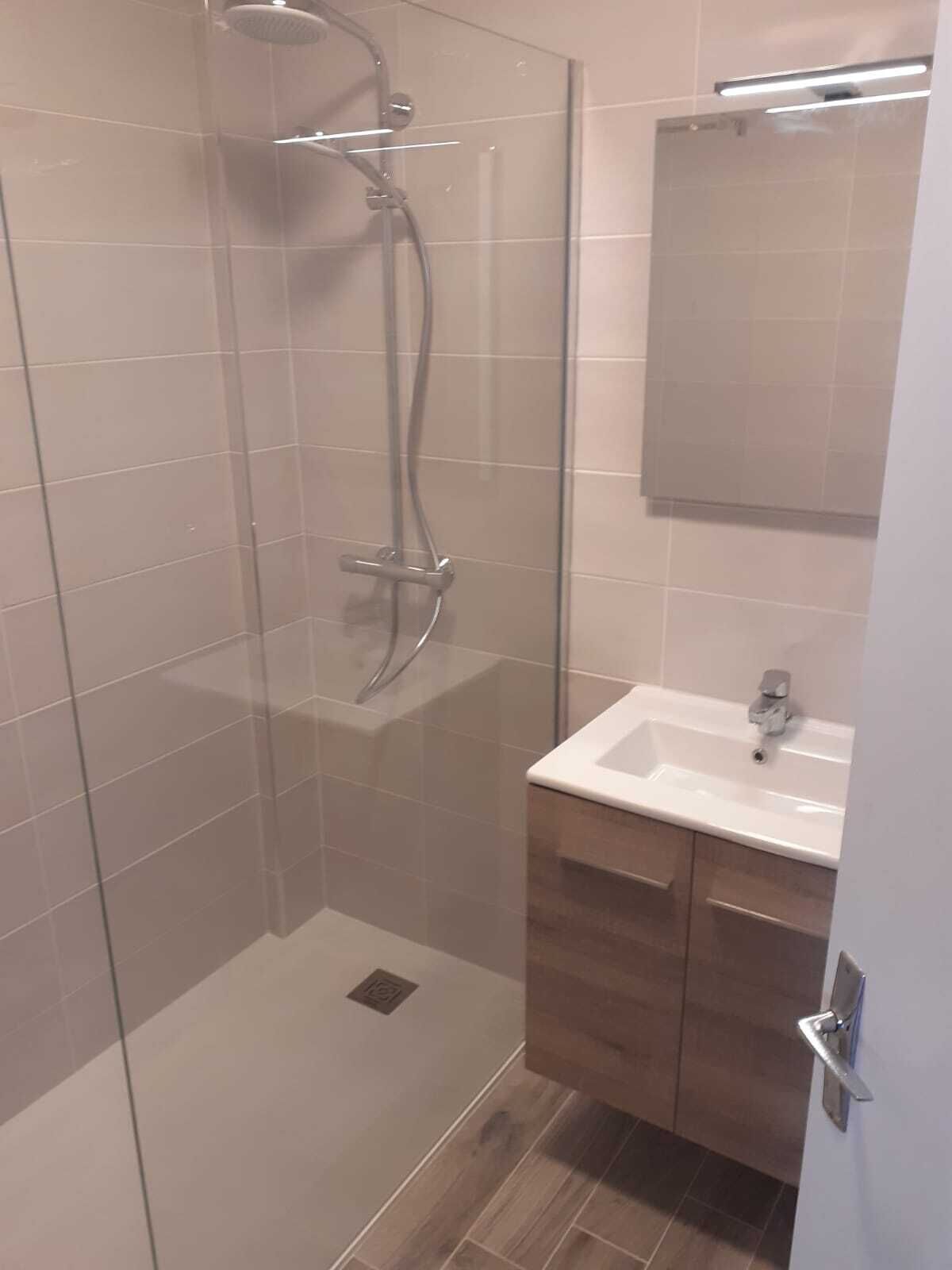 A modern bathroom with a glass-enclosed shower, a white sink, and wooden cabinets.