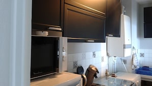 Una cocina moderna con armarios oscuros, microondas integrado y una mesa de vidrio.