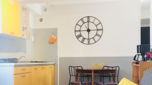 Ein kompakter Wohnbereich mit Küchenzeile, einem Essbereich mit Tisch und Stühlen sowie einer Couch mit gemustertem Bezug.
