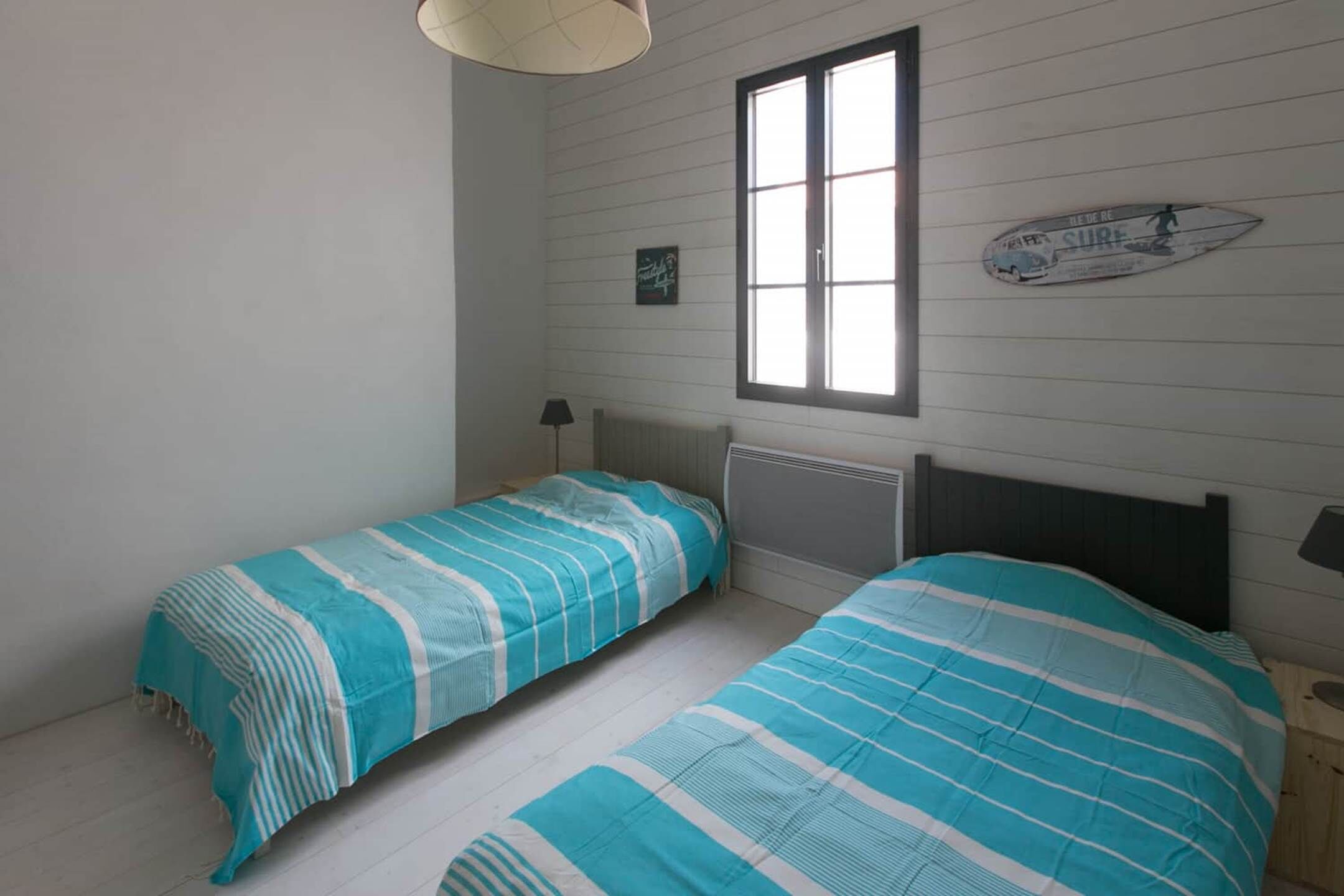 A room with two beds, a window, and a surfboard decoration on the wall.