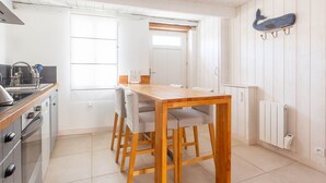A kitchen with a wooden table and chairs, a stove, and a white cabinet. - La Petite Maison (sleeps 4) (La Couarde-sur-Mer)