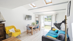 Uma sala de estar luminosa com sofá, poltrona amarela e área de jantar com mesa e cadeiras.