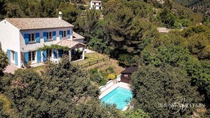 Ein zweistöckiges Haus mit Swimmingpool, umgeben von üppiger Vegetation und Hügeln.