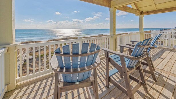 Eine Holzterrasse mit Adirondack-Stühlen mit Blick auf einen Strand.