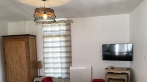 A living room with a wooden cabinet, a red chair, a wooden table, a television, and a patterned curtain.