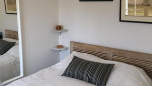 A bedroom with a large bed, a bedside table, a small shelf, and a framed picture on the wall.
