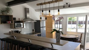 A modern kitchen with a central island, bar stools, a microwave, a stainless steel range hood, and hanging pendant lights.