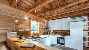 A modern kitchen with wooden beams, white cabinetry, and a large window.