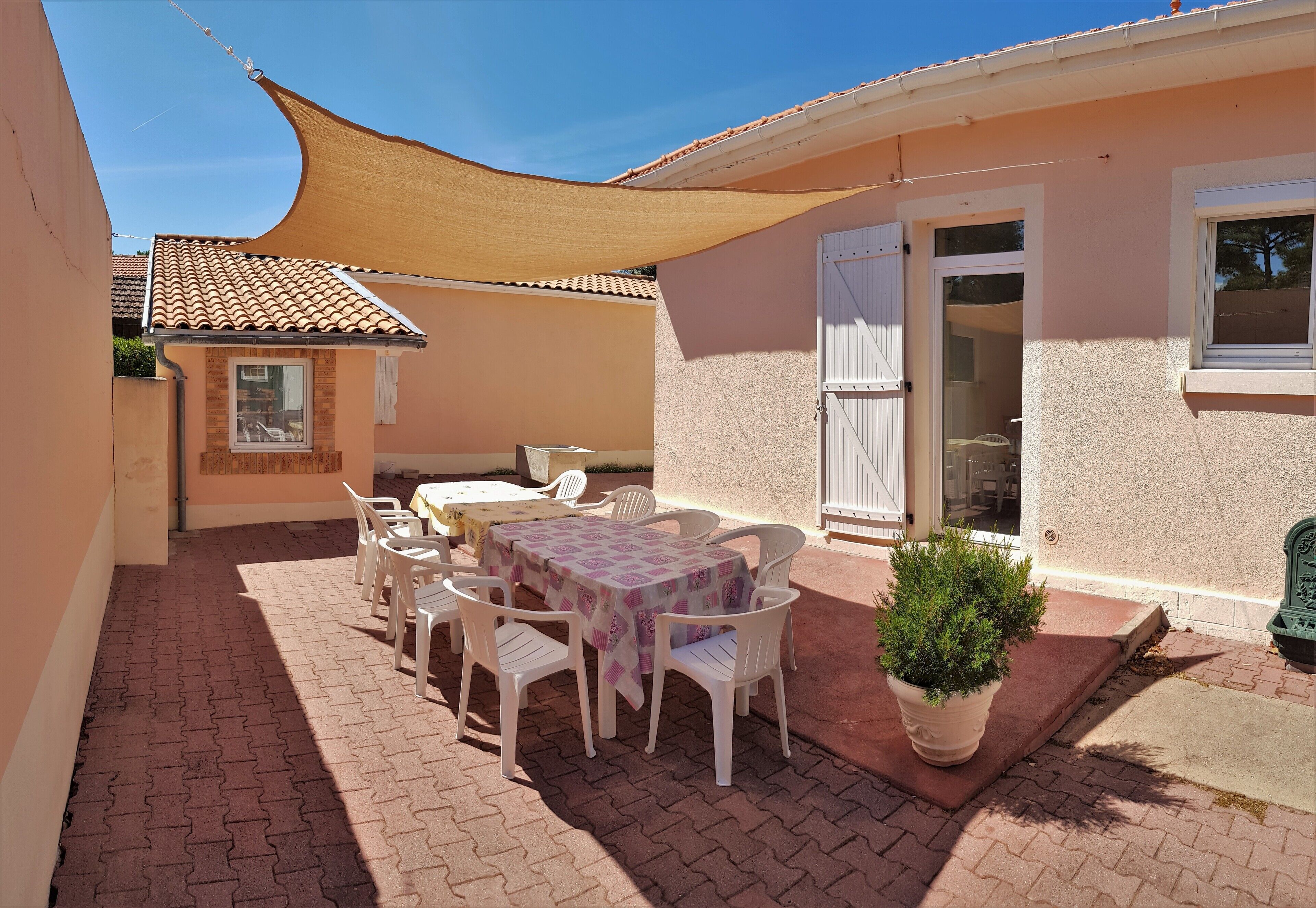 An outdoor patio with a table and chairs, a potted plant, and a building with a tiled roof and windows.