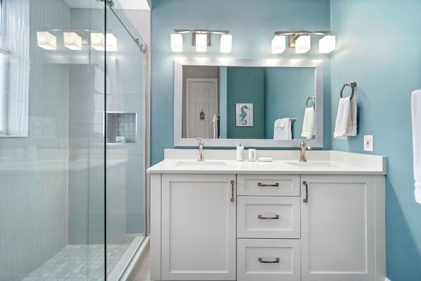 Un baño con cabina de ducha de vidrio, tocador blanco con un espejo grande y paredes color aguamarina.