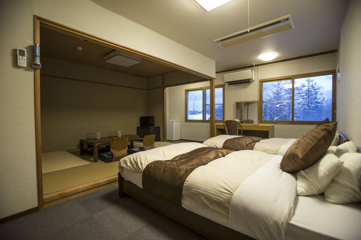 Habitación de hotel con cama, escritorio, silla y ventana con vistas a árboles.