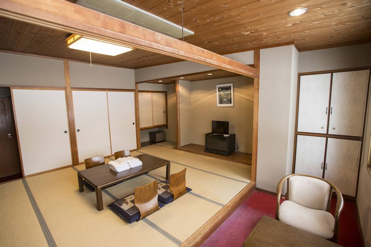 Una habitación japonesa tradicional con suelo de tatami, una mesa de madera baja, esteras de tatami, un televisor y un armario.