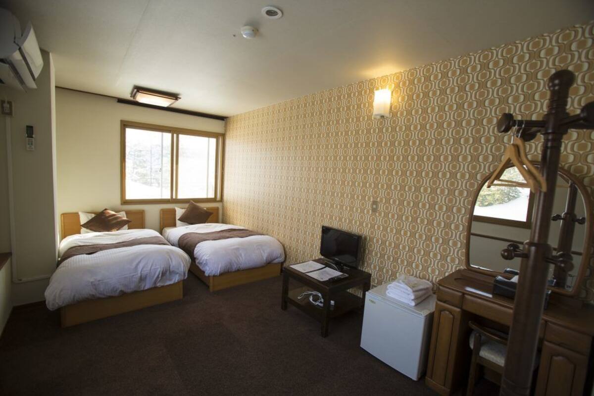 Habitación de hotel con dos camas, televisor, un pequeño escritorio, espejo y ventana.