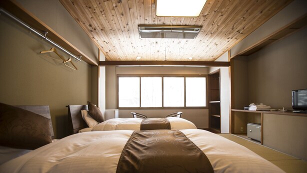A hotel room with two beds, a wooden ceiling, a large window, and a desk with a television. - Nomad Hakuba (Hakuba)
