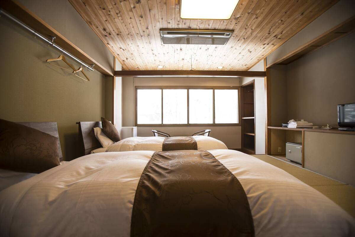 Habitación de hotel con dos camas, techo de madera, un ventanal grande y un escritorio con televisor.