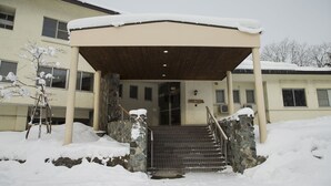 Un edificio con un vestíbulo cubierto, escalones de piedra y acumulación de nieve.