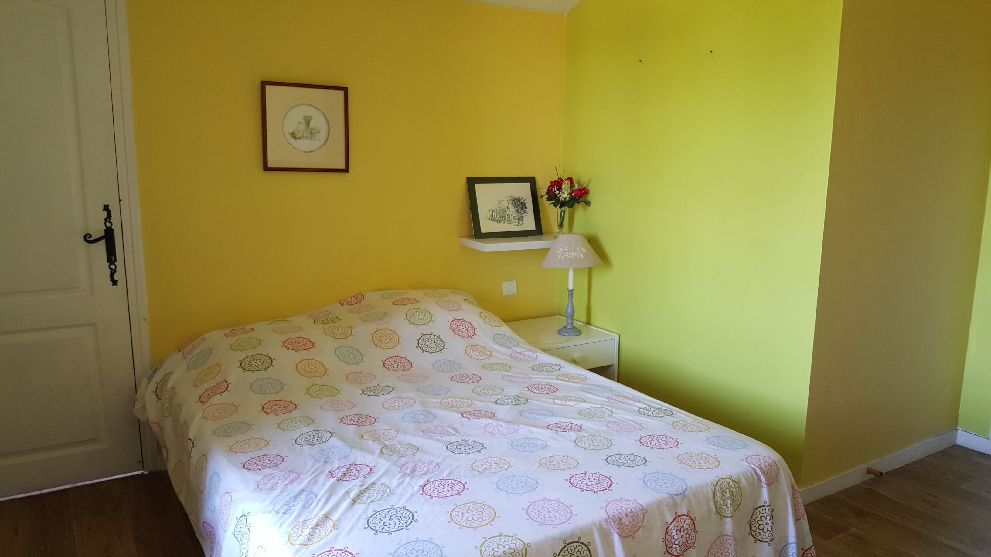 Una habitación con una cama, una mesita de noche, una lámpara y dos cuadros en la pared.