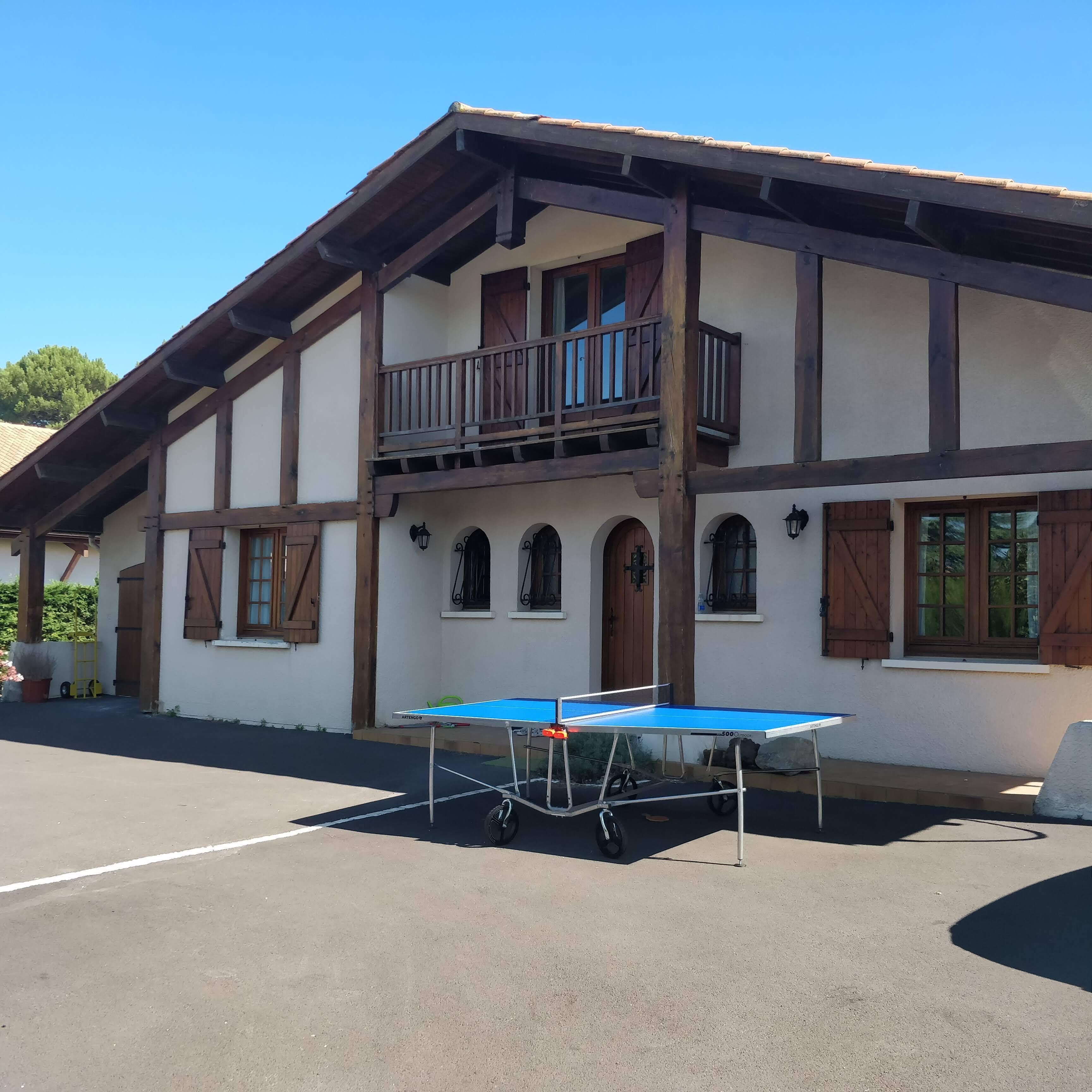 Een traditionele chalethut met een balkon, een tafeltennistafel en een verharde parkeerplaats.