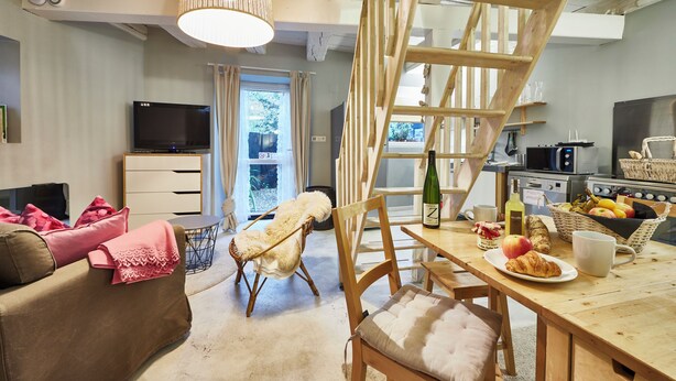 A cozy living room with a sofa, a chair, a dining table with breakfast items, a TV, and a staircase.