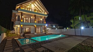 A two-story house with a swimming pool, a balcony, and a well-lit entrance. - Bali Style Self Catered Villas, Spacious 10BHK with Private Swimming Pool (Calangute)