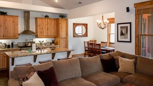 Un salón espacioso con un sofá grande color café, mesa de comedor de madera y una zona de cocina con armarios de madera y encimeras de granito.
