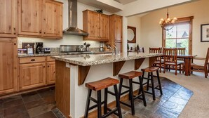 Una cocina con gabinetes de madera, encimeras de granito, campana extractora de acero inoxidable y una zona de bar con taburetes.
