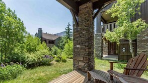 Una terraza de madera con sillas Adirondack, un pilar de piedra y vistas a un edificio con balcón.